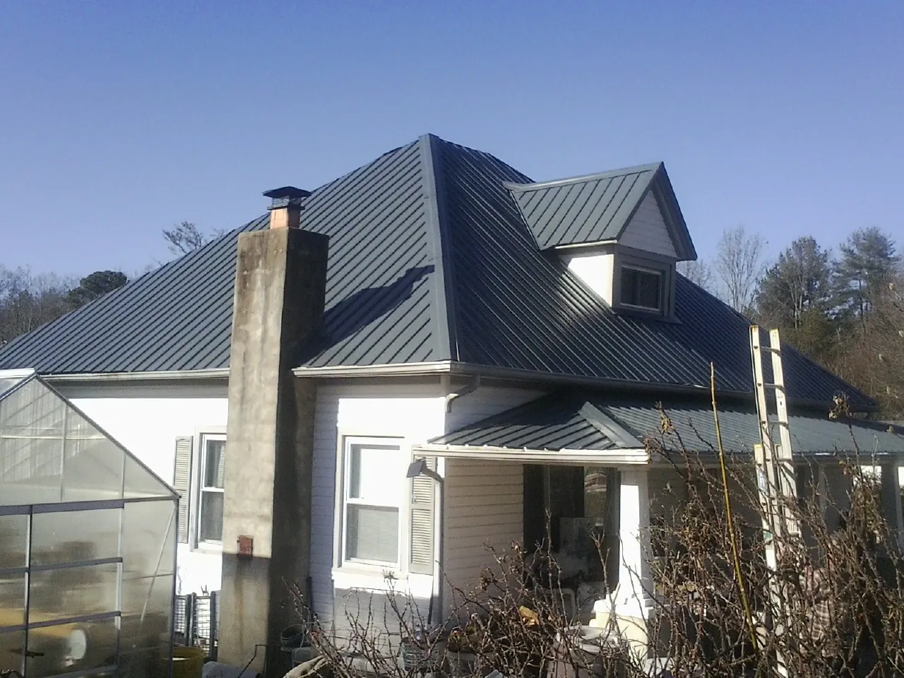 Dark blue standing seam metal roof on a white farmhouse with dormer — Slate & Tile Roof Repair by Roofing Brothers in Clarinda