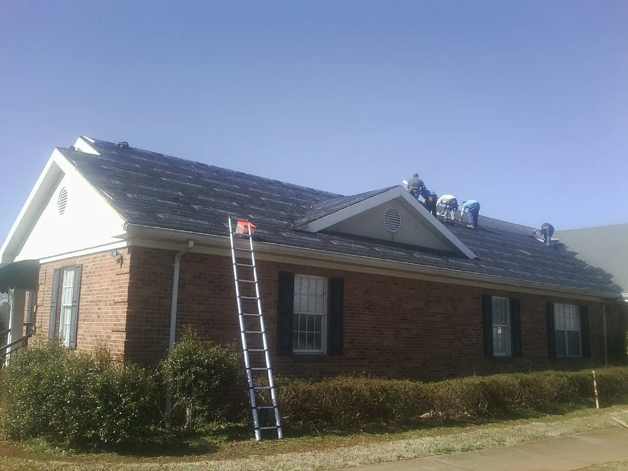 Crew tearing shingles off a brick ranch roof with a ladder set — Emergency Roof Repair work by our crew in Clarinda
