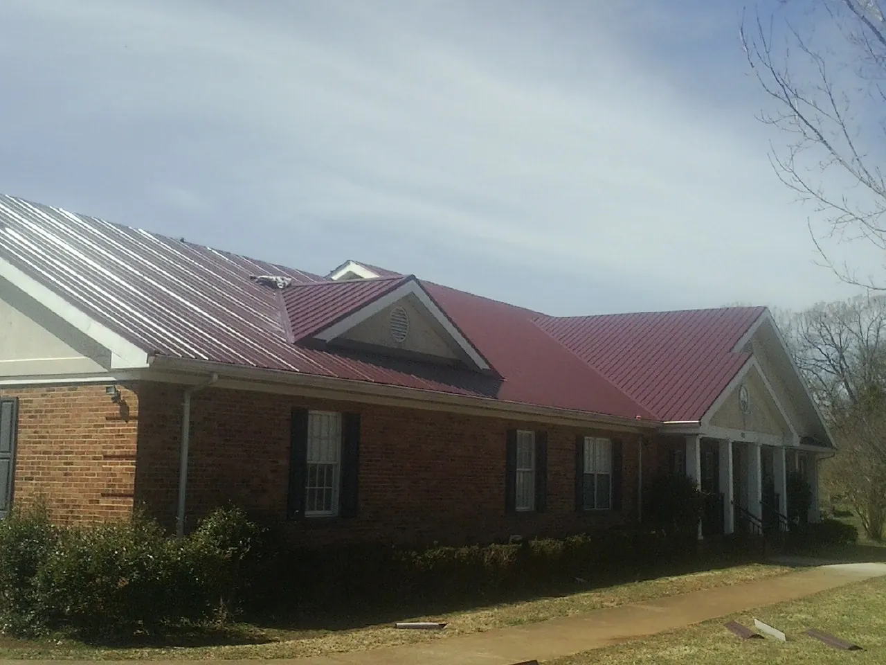 Red metal roof with gabled entries on a long brick building, from a Hail Damage Roof Repair job in Clarinda