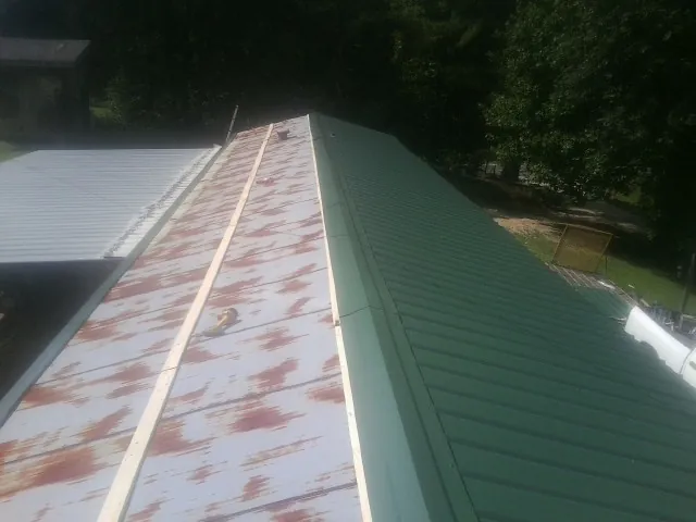 Old rusted panels beside newly installed green metal roofing — Wind Damage Roof Repair by Roofing Brothers in Clarinda