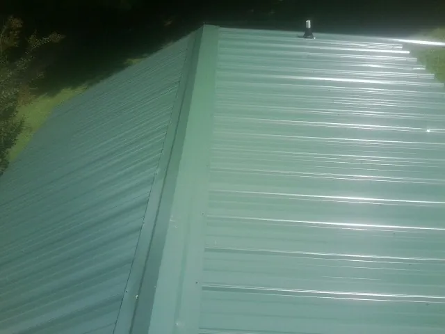 New green metal panels meeting at the ridge of a roof — Flat Roof Repair work by our crew in Clarinda