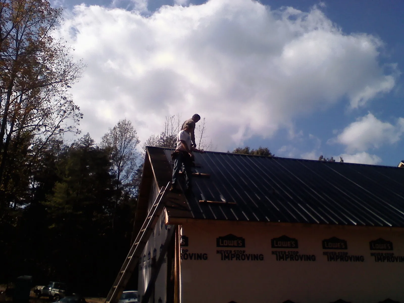 Roofer fastening dark metal panels high against a cloudy sky, from a Roof Inspection job in Clarinda