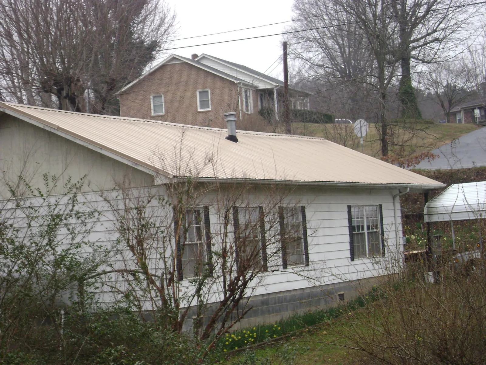 Tan metal roof on a white sided house set into a hillside — Commercial Roofing by Roofing Brothers in Clarinda