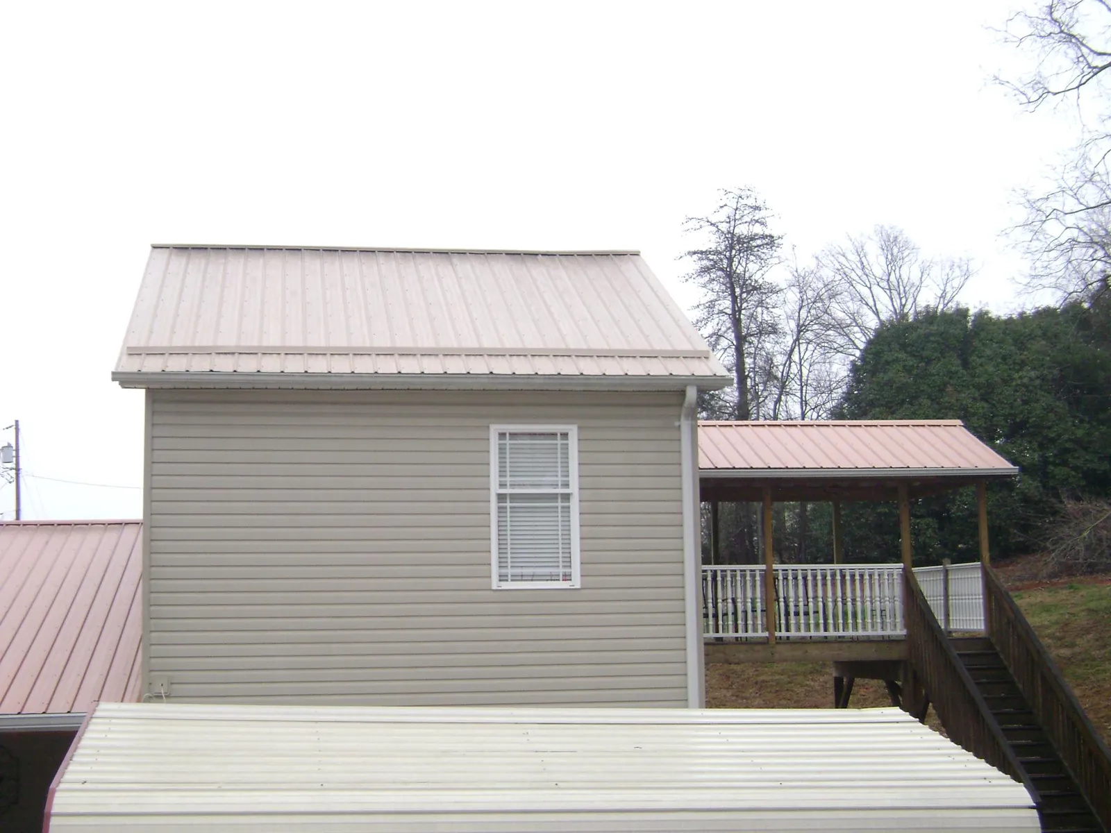 Tan metal roofs on a two story addition and attached porch, from a Roof Replacement job in Clarinda